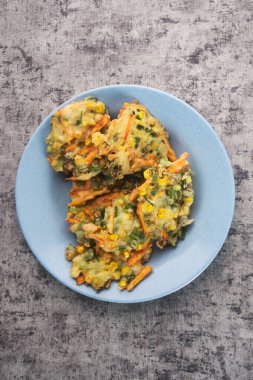 Lezzetli ev yapımı sebzeli börek, taze mısır, havuç ve yeşil soğan, mükemmel altın ve çıtır çıtır. Açık mavi bir seramik plaka üzerinde sunuluyor. Kır cazibesini arttıran gri bir arka planı var.