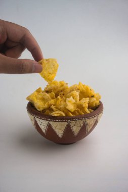 Beyaz bir yüzeye yerleştirilmiş bir kase cipsten mısır cipsi alan bir elin yakın çekimi. Atıştırma anlarını ve geleneksel toprak kabı tasarımı.