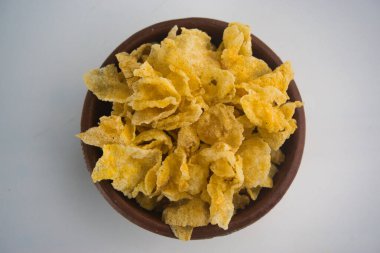 Parlak sarı çıtır mısırlı atıştırmalıklar dekoratif topraktaki kil kasede sunuluyor. Kültürel bir cazibeyle hoş bir ziyafetin özgün ve sanatsal sunumunu yapıyor.