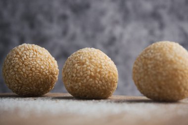 Kırsal ahşap bir yüzeye tozlu dekorasyonla yerleştirilmiş lezzetli susamlı hamur işleri. Doku ve detaylara odaklanarak yakalanan bu resim, aşçılık estetiği ve basitliği vurguluyor