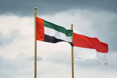 Flags of the United Arab Emirates and Indonesia fly on golden poles against a cloudy background, symbolizing international relations, unity, and cultural representation. A dynamic image depicting national pride and global connection clipart