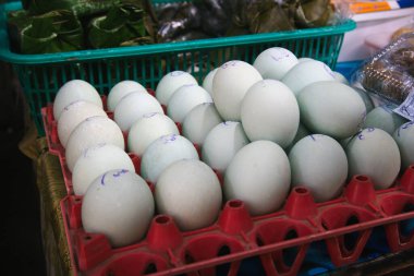 Taze tuzlanmış ördek yumurtalarıyla dolu bir tepsinin yakından görüntüsü. Yumurtalar, pürüzsüz dokularını ve mavimsi renklerini vurgulayan kırmızı bir plastik tutacağa yerleştirilmiş.