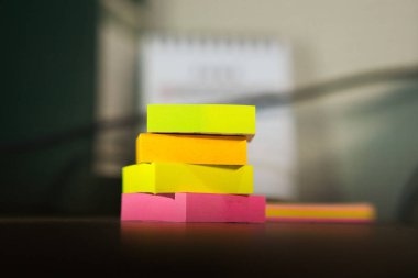 Ahşap bir masanın üzerine düzgünce istiflenmiş renkli yapışkan notlar. Ofis veya yaratıcı işler için ideal. Bu yapışkan notlar, iş ortamlarında üretkenliği, yaratıcılığı ve etkili planlamayı simgeler.