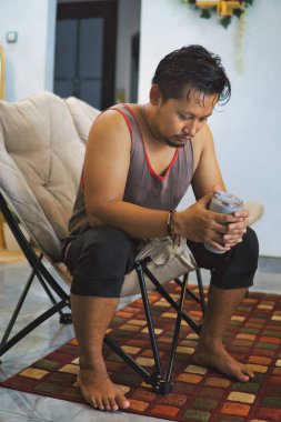 Bir erkek egzersiz seansından sonra oturma odasında dinlenir. Sütlü proteinini yudumlayarak evde sağlıklı ve aktif bir yaşam tarzını temsil eder.