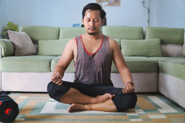 Huzurlu bir ev ortamında bacak bacak üstüne atarak meditasyon yapan bir adam farkındalık ve rahatlamayı teşvik eder..