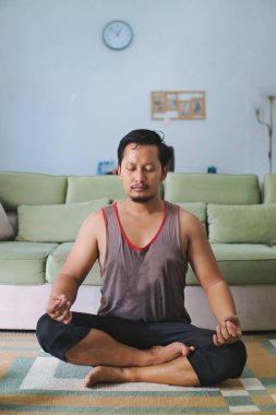 Huzurlu bir ev ortamında bacak bacak üstüne atarak meditasyon yapan bir adam farkındalık ve rahatlamayı teşvik eder..