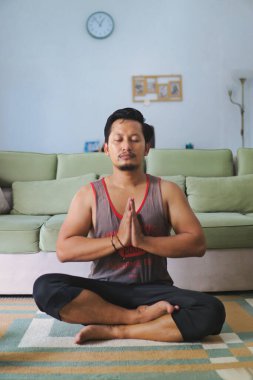 Huzurlu bir ev ortamında bacak bacak üstüne atarak meditasyon yapan bir adam farkındalık ve rahatlamayı teşvik eder..
