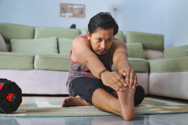 Oturma odası ortamında, esneklik ve uygunluğa odaklanmış, oturma odasında egzersiz yapan bir adam. Görüntü evde egzersiz rutinlerini ve sıradan bir ortamda sağlıklı bir yaşam tarzını vurgular.