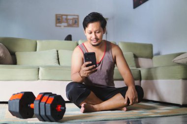 Halının yanında halı üzerinde otururken akıllı telefon kullanan bir adamın rahatlama ve zindelik unsurlarını vurguladığı bir iç mekan seti