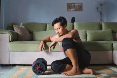 Egzersizden sonra dinlenen bir adam evinin oturma odasında dambılları kaldırıyor.