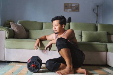 Egzersizden sonra dinlenen bir adam evinin oturma odasında dambılları kaldırıyor.