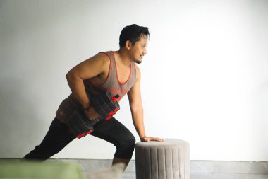 Odaklanmış bir birey, içeride bir tabure desteğiyle bir dambıl kullanarak güç çalışması yapar.