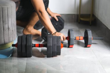 Bir kattaki ayarlanabilir ağırlıkların yakın plan görüntüsü, onları egzersiz için düzenleyen bir bireyin yanı sıra, evde spor yapmanın özünü yakalamak ve güç antrenmanı faaliyetleri için kararlılık