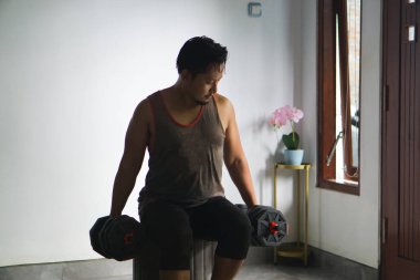 Ağır dambılları kararlı bir şekilde kaldırırken evde bireysel güç antrenmanı yapıyor.