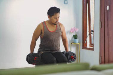 Ağır dambılları kararlı bir şekilde kaldırırken evde bireysel güç antrenmanı yapıyor.