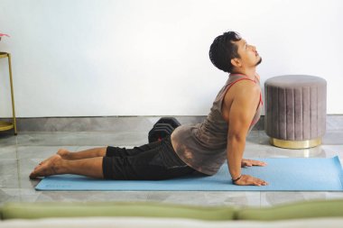 Evde yoga yapan bir adam yoga minderinde kobra pozu veriyor. Çevre huzurlu ve rahattır, kondisyon uygunluğu, sağIık ve kapalı alanda dikkatli bir egzersiz.
