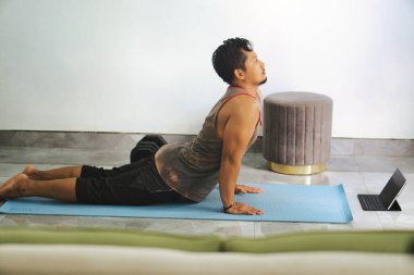 Evde yoga yapan bir adam yoga minderinde kobra pozu veriyor. Çevre huzurlu ve rahattır, kondisyon uygunluğu, sağIık ve kapalı alanda dikkatli bir egzersiz.
