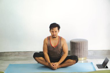 Yoga minderinde bacak bacak üstüne atmış bir adam, minimalist bir iç mekanda farkındalık ve rahatlama egzersizi yapıyor..
