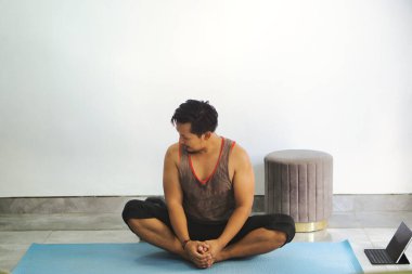 Yoga minderinde bacak bacak üstüne atmış bir adam, minimalist bir iç mekanda farkındalık ve rahatlama egzersizi yapıyor..