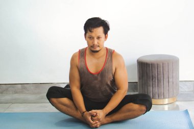 Yoga minderinde bacak bacak üstüne atmış bir adam, minimalist bir iç mekanda farkındalık ve rahatlama egzersizi yapıyor..