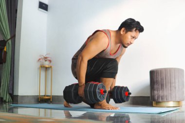 Kol halterleri kullanarak içeride egzersiz yapan motive olmuş bir birey. Bir ev ortamında kendini adamanın, sağlığın ve kendini geliştirmenin özünü yakalar.