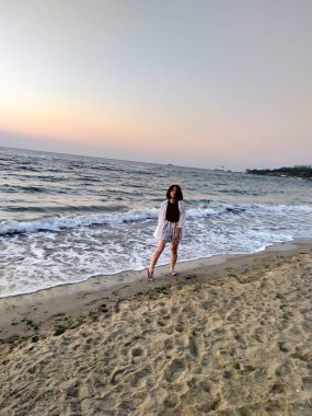 Gün doğarken deniz kenarındaki beton iskelede gezinen bir kadının arka görüntüsü. Seyahat, özgürlük ve yaz tatili kavramı. Gün doğumunda ufka doğru ilerleyen deniz kadınının huzurlu sabah yürüyüşü, özgürlük ve huzurun tadını çıkarıyor.