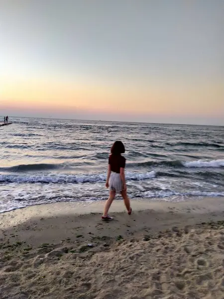 Gün doğarken deniz kenarındaki beton iskelede gezinen bir kadının arka görüntüsü. Seyahat, özgürlük ve yaz tatili kavramı. Gün doğumunda ufka doğru ilerleyen deniz kadınının huzurlu sabah yürüyüşü, özgürlük ve huzurun tadını çıkarıyor.