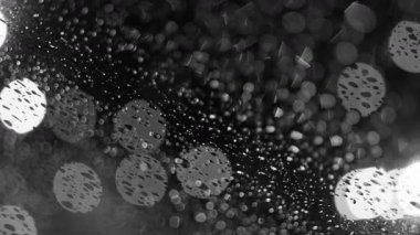Yağmur damlaları arkaplandaki bulanık ışıklarla aydınlanan cam bir yüzeye nazikçe tutunur.