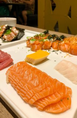 Suşi ve somon balığı, ton balığı, beyaz balık ve arkaplanda temaki olan mürekkep balığıyla dolu bir restoran masası..