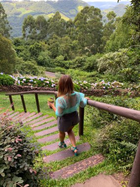 Dağlarda tatilde ya da tatilde dinlenen ve baca içen bir kadın mavi gökyüzü, bulutlar ve dağlarda bir sürü yeşil ağaçla birlikte açık havada bir kanepede uzanır..