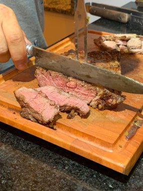 Barbecue meat cooked to medium-rare being cut with a rustic gaucho knife on top of a wooden cutting board. clipart