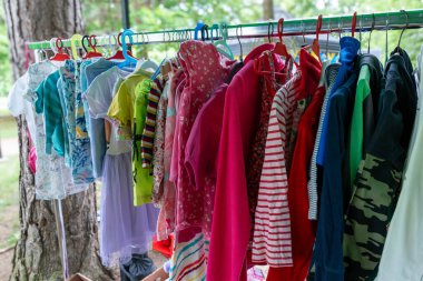 Parlak çocuklar elbise askılarında farklı şekillerde giyinirler. Ağaçların ve doğanın yakınındaki elbise değiş tokuşu sürdürülebilirlik kavramı ve aile dostu yeniden kullanım kültürü.