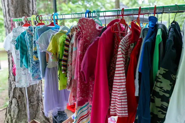 Parlak çocuklar elbise askılarında farklı şekillerde giyinirler. Ağaçların ve doğanın yakınındaki elbise değiş tokuşu sürdürülebilirlik kavramı ve aile dostu yeniden kullanım kültürü.