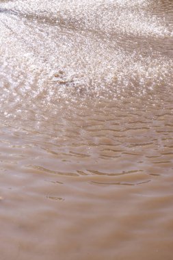 Kahverengi su yüzeyi dalgalanma dokusu dikey. Sabahları dalgalı suyun doku arkaplanı. Doğadaki güzellik, küçük dalgalar, güneş ışığı, manzara, duvar kağıtları için yaz konsepti. Su yüzeyi dokusu.