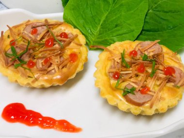 Ispanak yaprağı ve sosla süslenmiş sosis ve peynirli mini Quiche Lorraine.