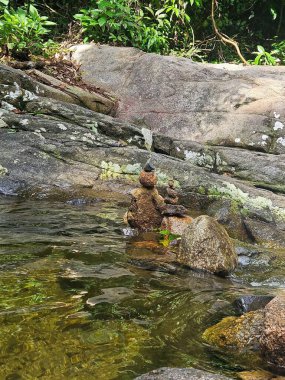 Etrafı yemyeşil bitki örtüsü ve yosun kaplı kayalarla çevrili, sakin bir derenin kenarına istiflenmiş güzel taş heykeller. Sahne, doğayla uyum ve sükunet hissi uyandırıyor..