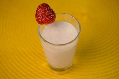 Canlı kırmızı çilekli kremalı çilekli smoothie, neşeli bir dokunuş için parlak sarı bir arka planda servis.