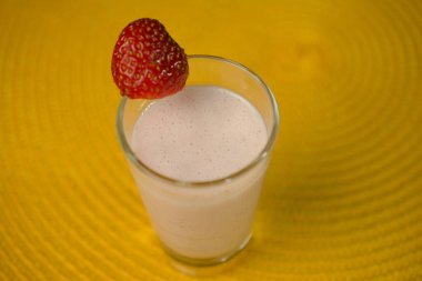 Taze çilekli kremalı çilekli smoothie, canlı sarı bir arka planda servis edilir..