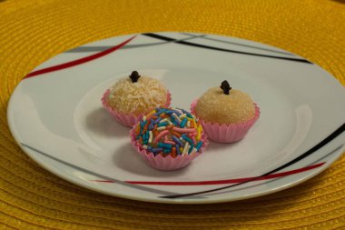 Beyaz bir tabakta üç tugay askerinin yakın plan fotoğrafı. Kırmızı ve siyah detaylar. Renkli serpiştirilmiş, biri hindistan cevizi talaşlı ve diğeri karanfil süslemeli şekerle tozlanmış..