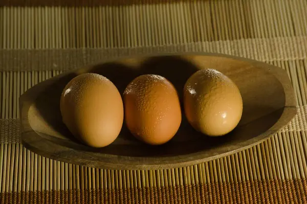 Tahta bir kâse içinde, bambu bir hasırın üzerine yerleştirilmiş kahverengi yumurta üçlüsü. Kahverenginin değişik tonları ve yumurtaların üzerindeki yoğunluk dokunsal ve organik bir his veriyor. Yumuşak ışıklandırma nazikçe atıyor.