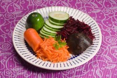 İçinde rendelenmiş havuç, dilimlenmiş salatalık, pancar ve taze yeşillikler olan canlı bir tabak. Sağlıklı ve renkli bir salata için mükemmel bir kombinasyon..