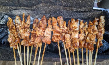 Kömürün üstünde ızgara yapan tavuk şişleri. Tavuk parçaları terbiye edilip altın sarısı bir kahverengiye dönüştürülüyor ve sulu ve lezzetli bir görünüm sergiliyor. Şişler düzgünce dizilmiş, lezzetli ve iştah açıcı bir sahne çağrıştırıyor..