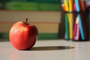 Okul masasında bir elma. Pencereden gelen ışık sınıfı sular altında bırakır ve güzel gölgeler bırakır. Seçici odak.