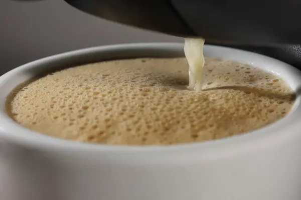 Kahve makinesinden akan bir dere bir fincan kahveyi kremayla doldurur..