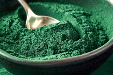 Siyah bir kâsede kaşıkla yeşil spirulina tozu.
