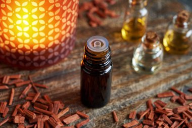 Kırmızı sanalwood cipsleri ve arka planda mum ışığı olan koyu renk bir aromaterapi şişesi.