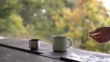 Hand taking a metal cup with steaming tea during a tourist trip in autumn