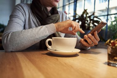 Woman sitting at a cafe, having coffee and working on her mobile phone
