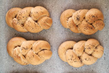 Four rreshly baked braided bread buns made from whole grain spelt flour, sprinkled with poppy seeds