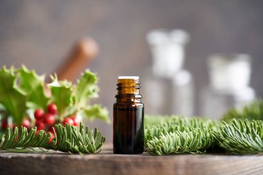 A dropper bottle of aromatherapy essential oils with fir branches and holly on a table